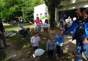 Rodzice z dziećmi stoją z balonami na świeżym powietrzu podczas pikniku.